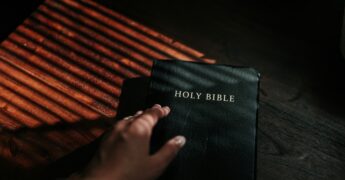 A hand resting on an open Bible, symbolizing faith, reflection, or prayer.