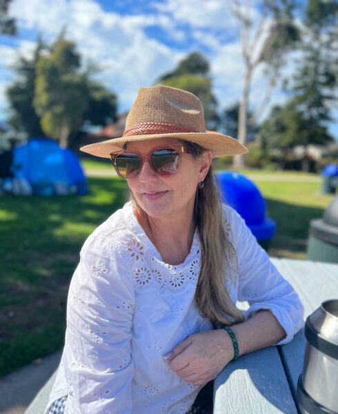 Photo of woman with sunglasses and hat looking to side smiling.