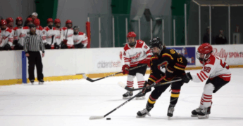 Students playing hockey in an indoor hockey rink.