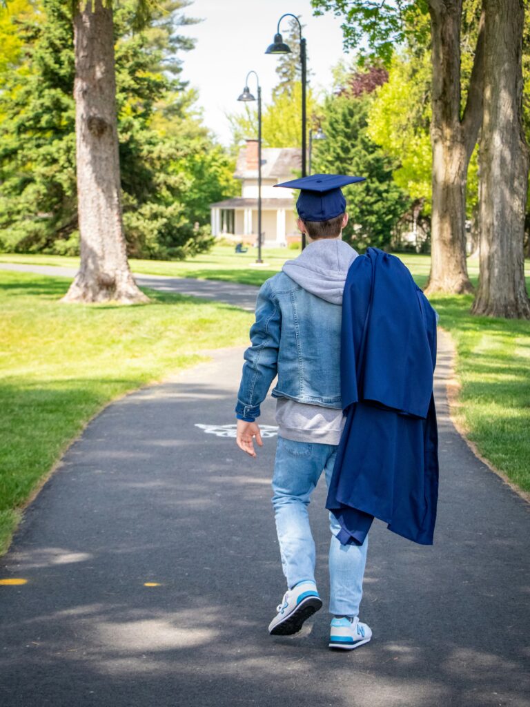 Male student walking on path with graduation cap and gown.